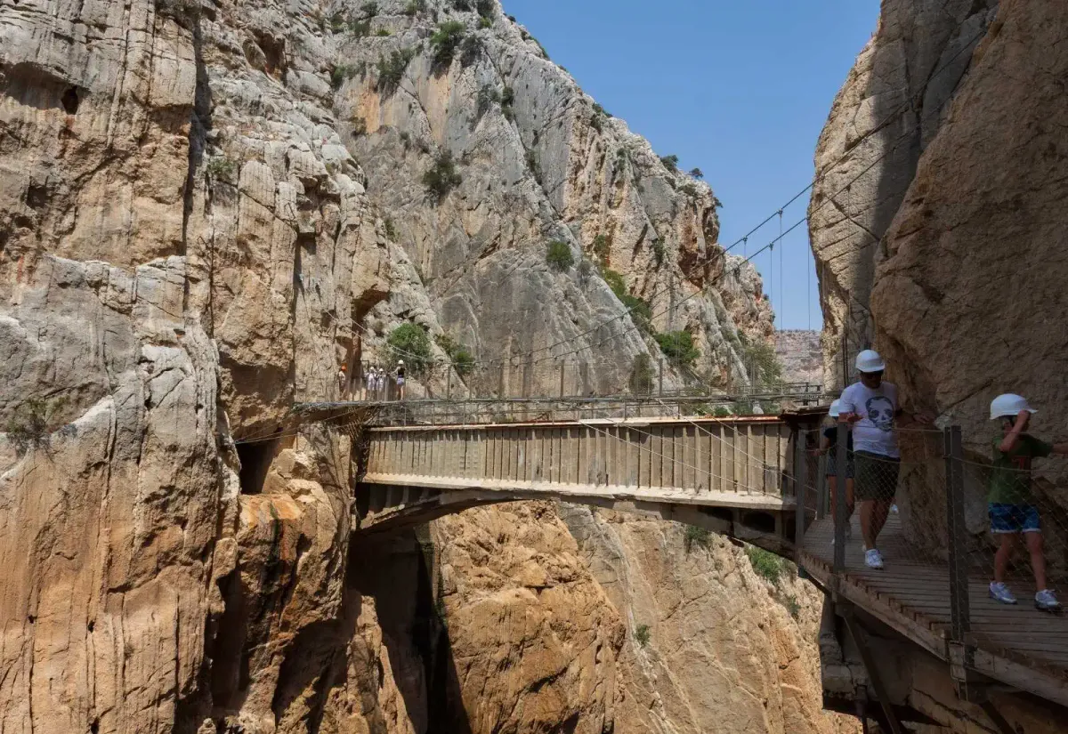 People crossing the Caminito del Rey bridge wearing helmets